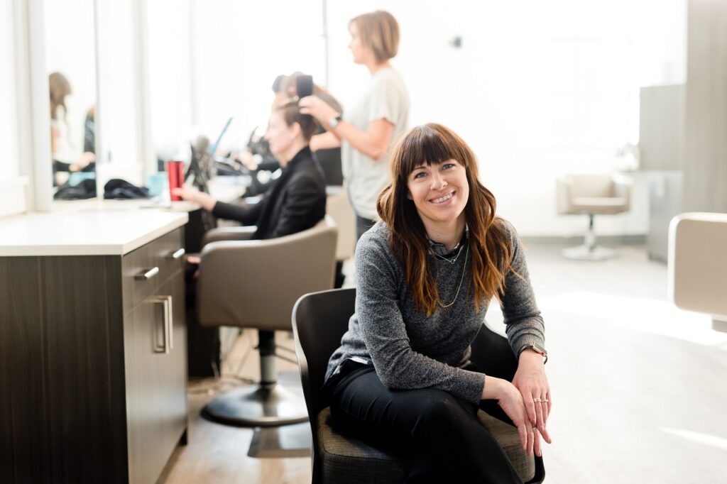a sole trader who smiles before a camera while a client is getting a hair treatment