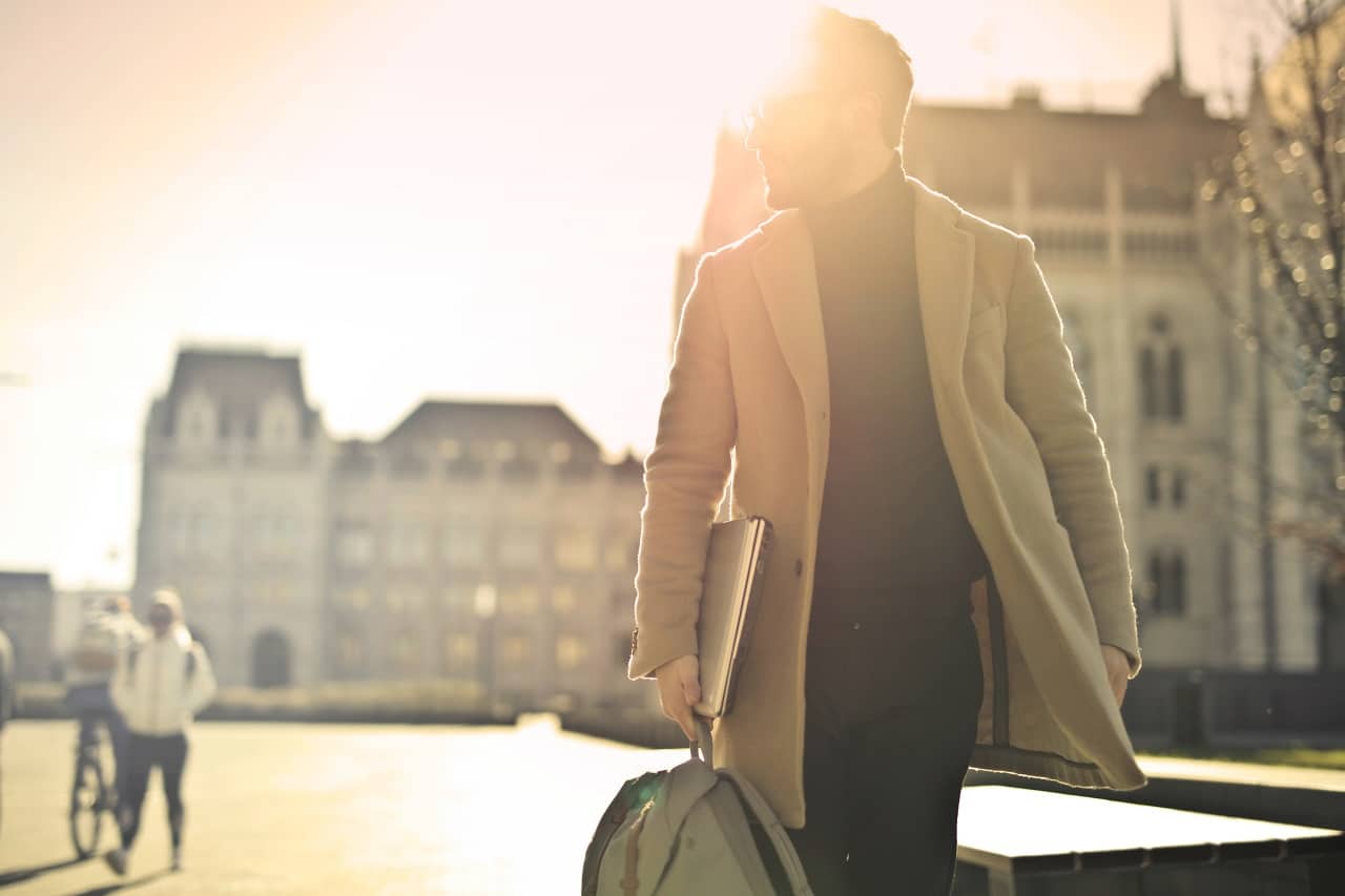 a businessman carrying a laptop and walking on the streets under broad daylight