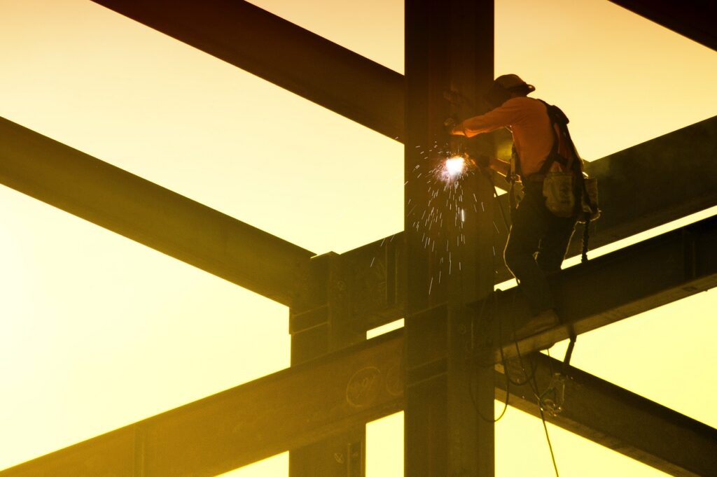 welding sparks as a welder works on a huge steel at a building construction site as the sun is setting
