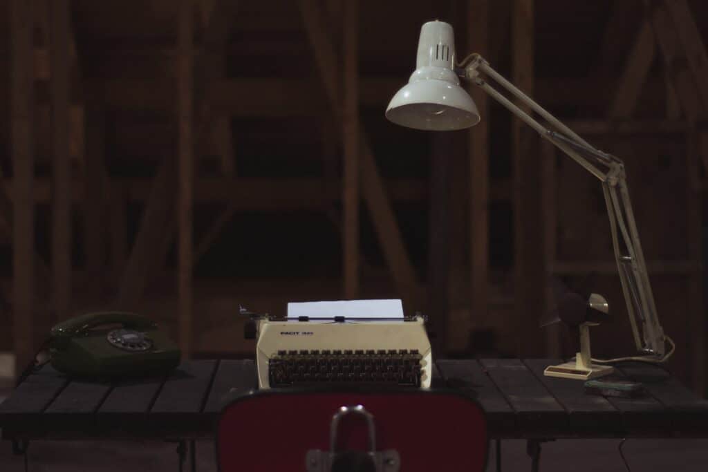a classic work station with a loaded typewriter, a white desk lamp, and a red telephone