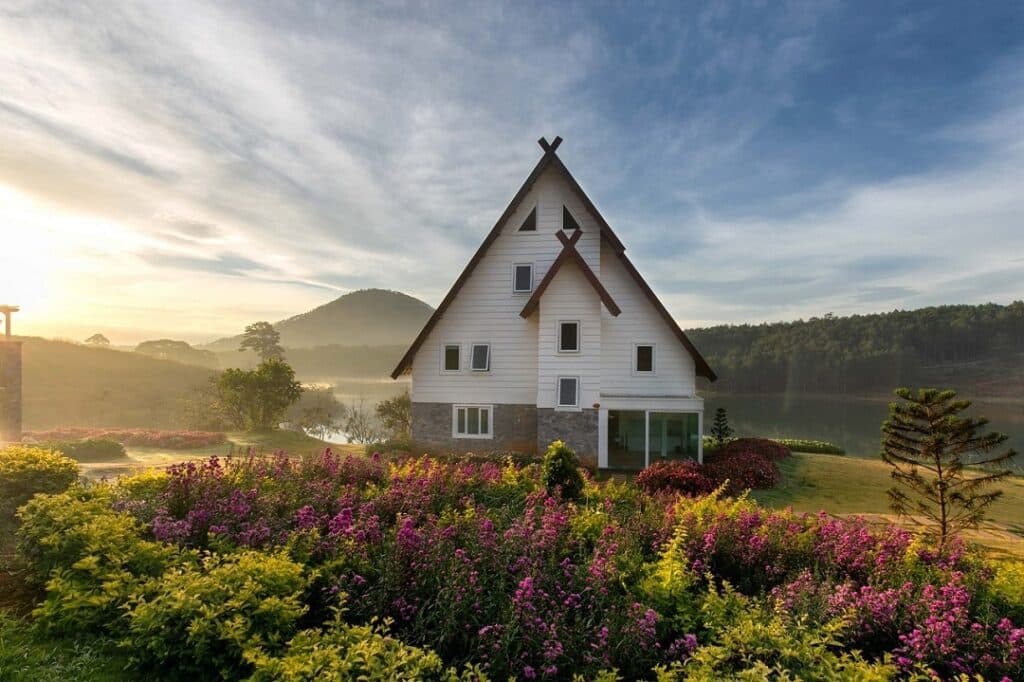 a barn-type house sitting placidly on a green and flowery loan with the morning fog clearly receding