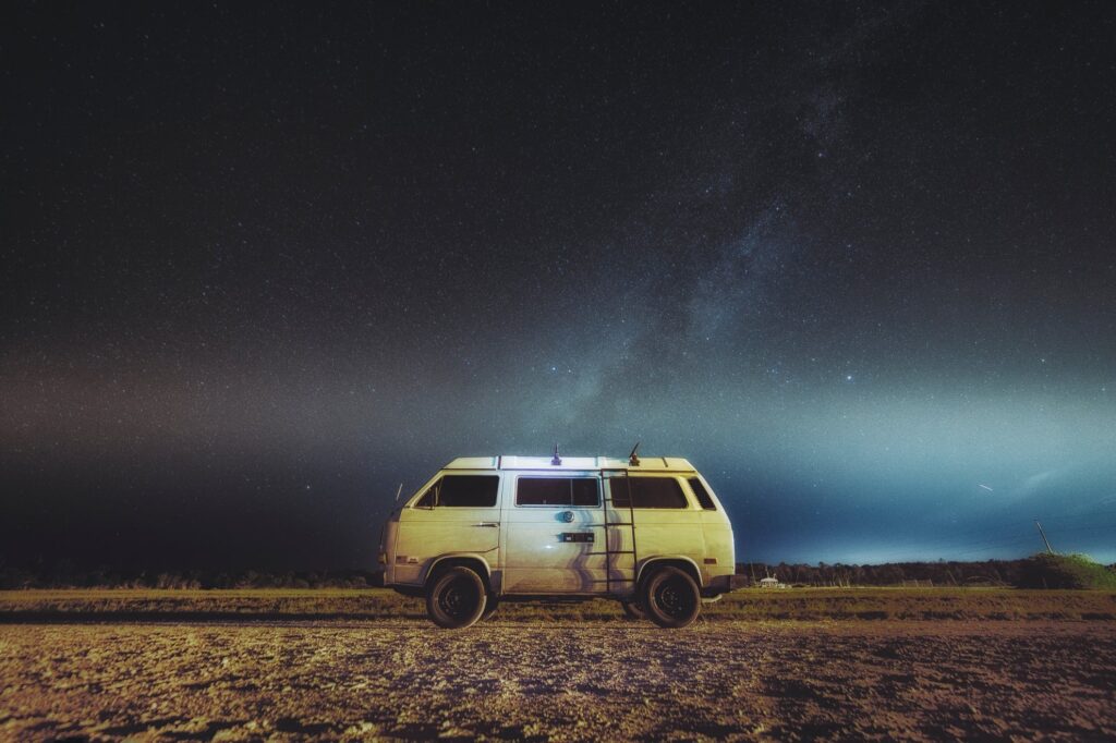 a camping van parked under a starry night and against a panoramic background