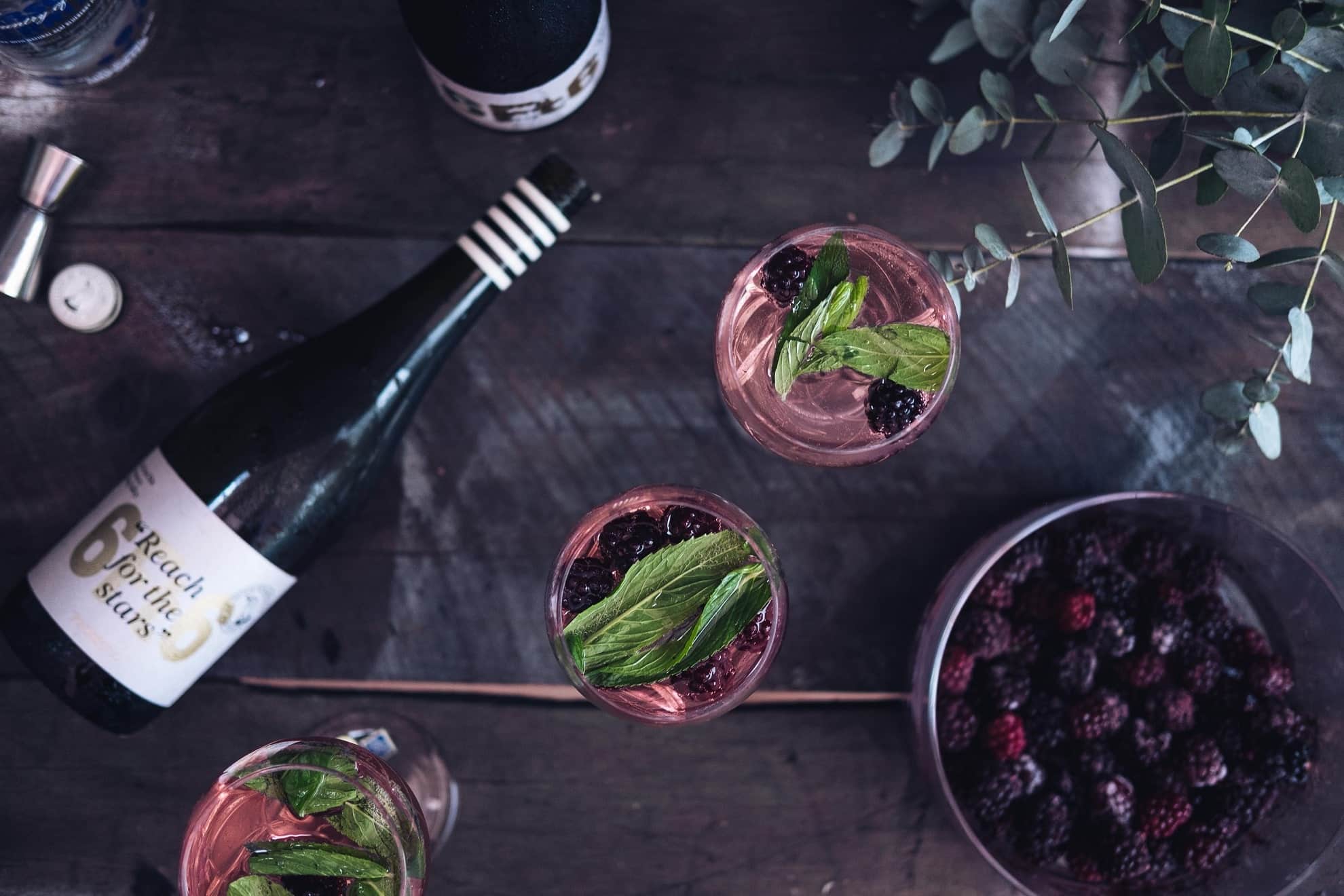 a bottle of wine, three wine glasses, and a bowl of blueberries