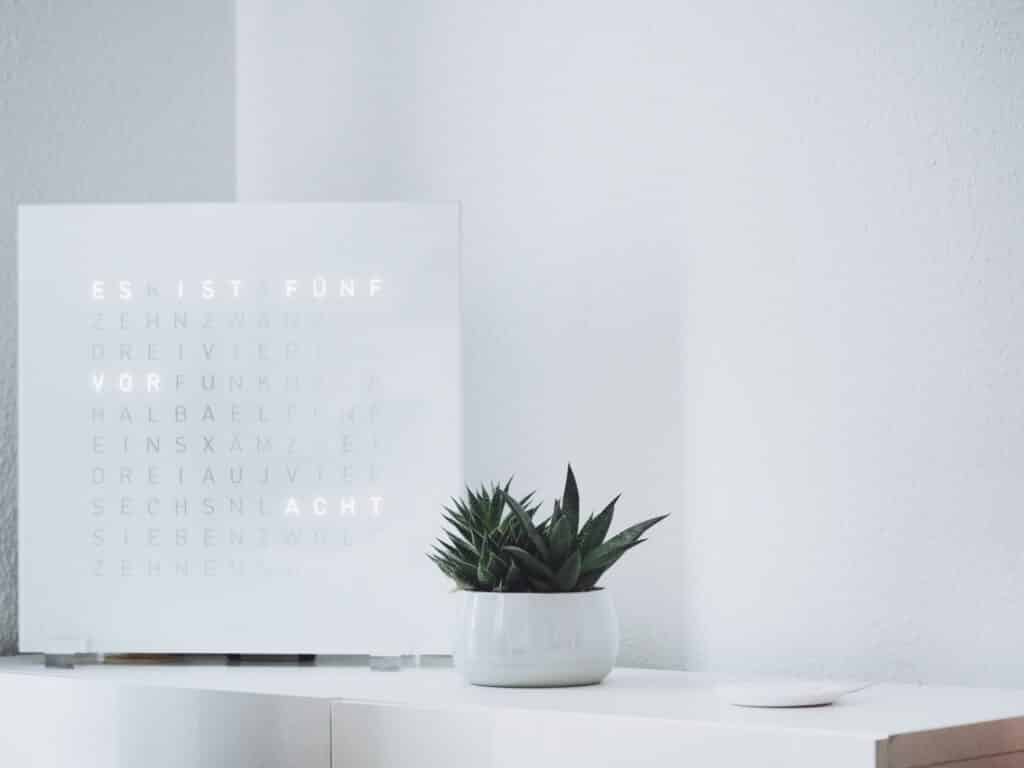 a white desk with a white digital calendar and white flower vase with a cactus plant