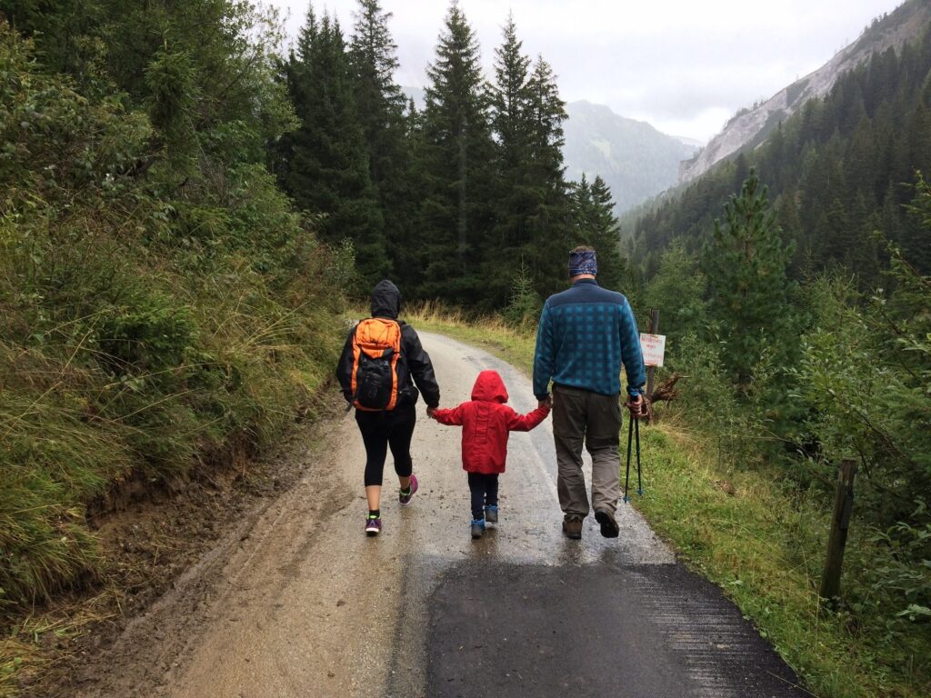 a man, woman, and their child walking along a dirt road while enjoying the forest view