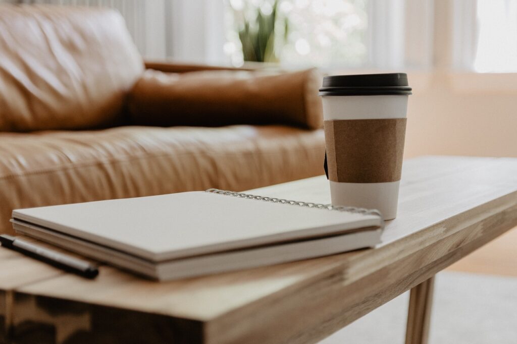 white and black coffee mug with a notebook and a pen on a coffee table