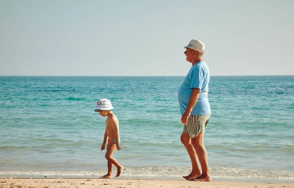 a grandfather following his grandson along the shores of the beach