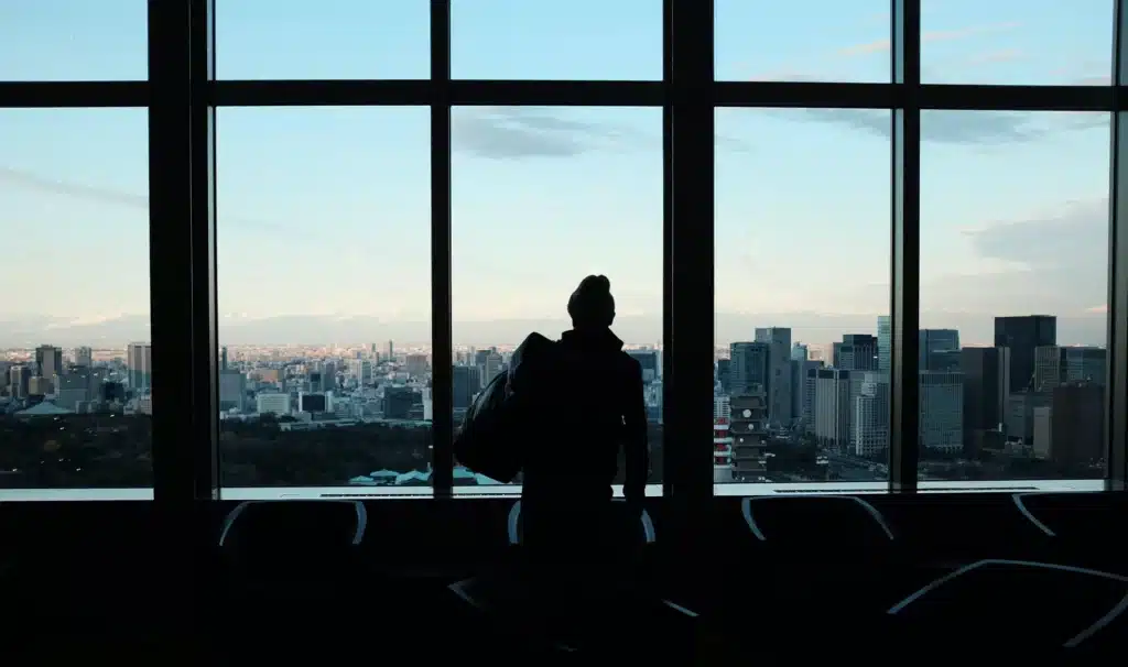 a woman holding a travel bag and looking through the large windows of the city skyline
