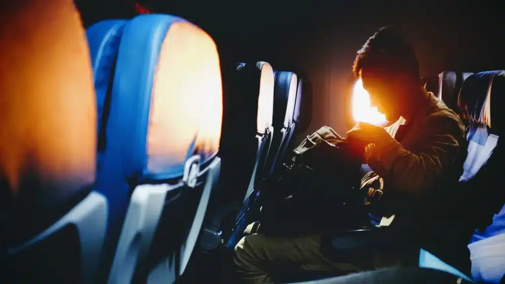 A passenger going through his carryon while the sun sets by his seat window, representing the concept of tax deductions for flight attendants.