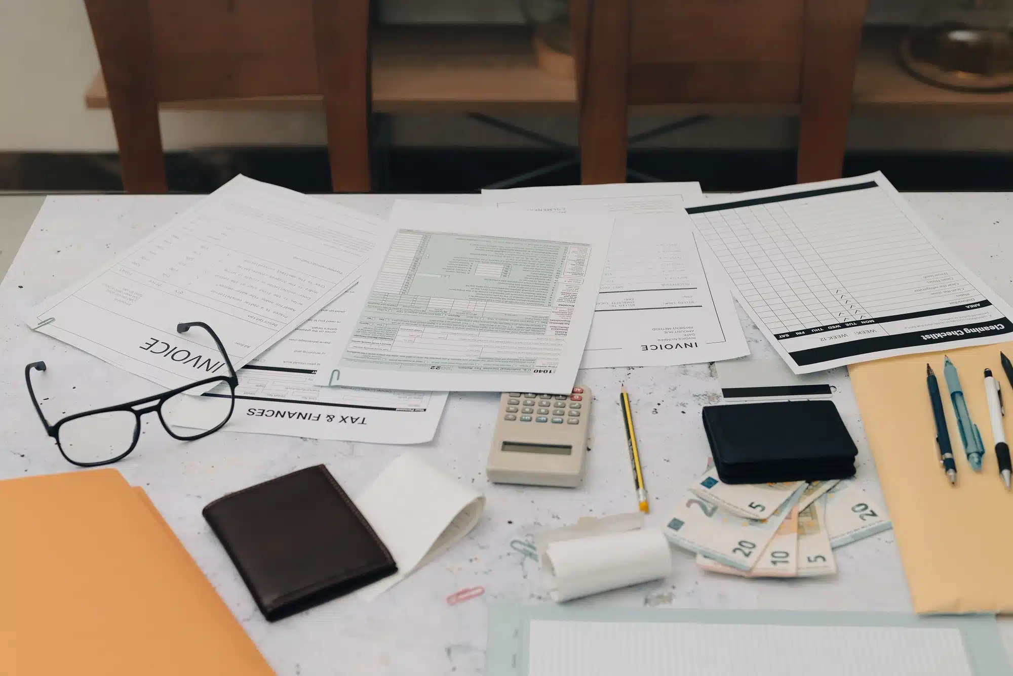 A table topped with invoices and tax forms, pens, and cash.