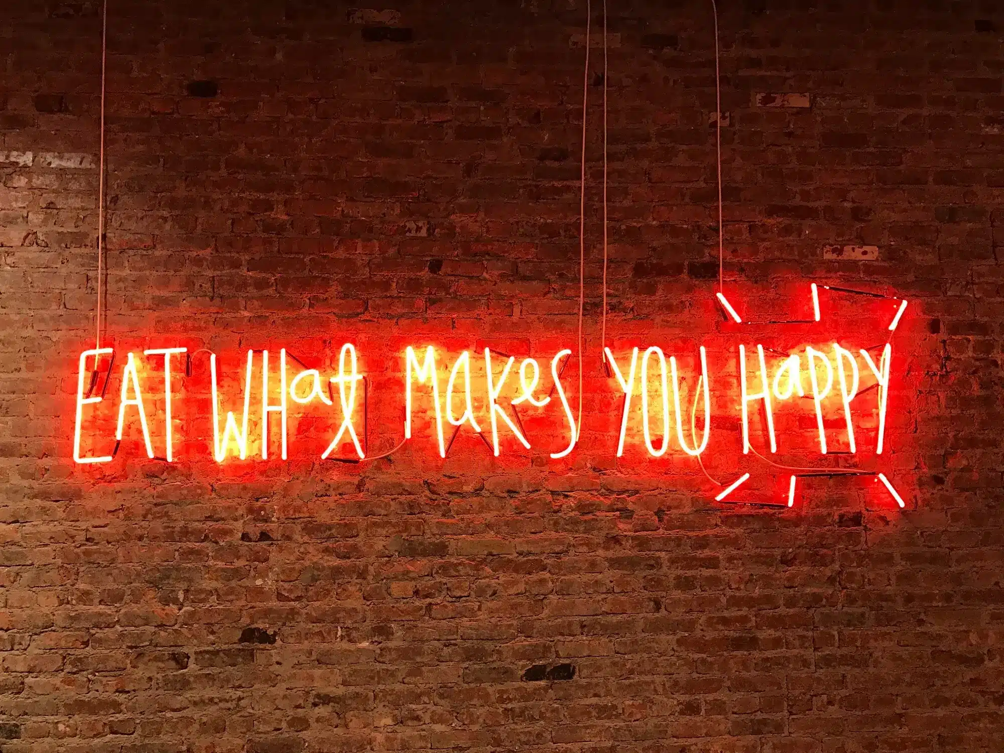 Neon light signage that says 'Eat what makes you happy,' representing the concept of GST on food.