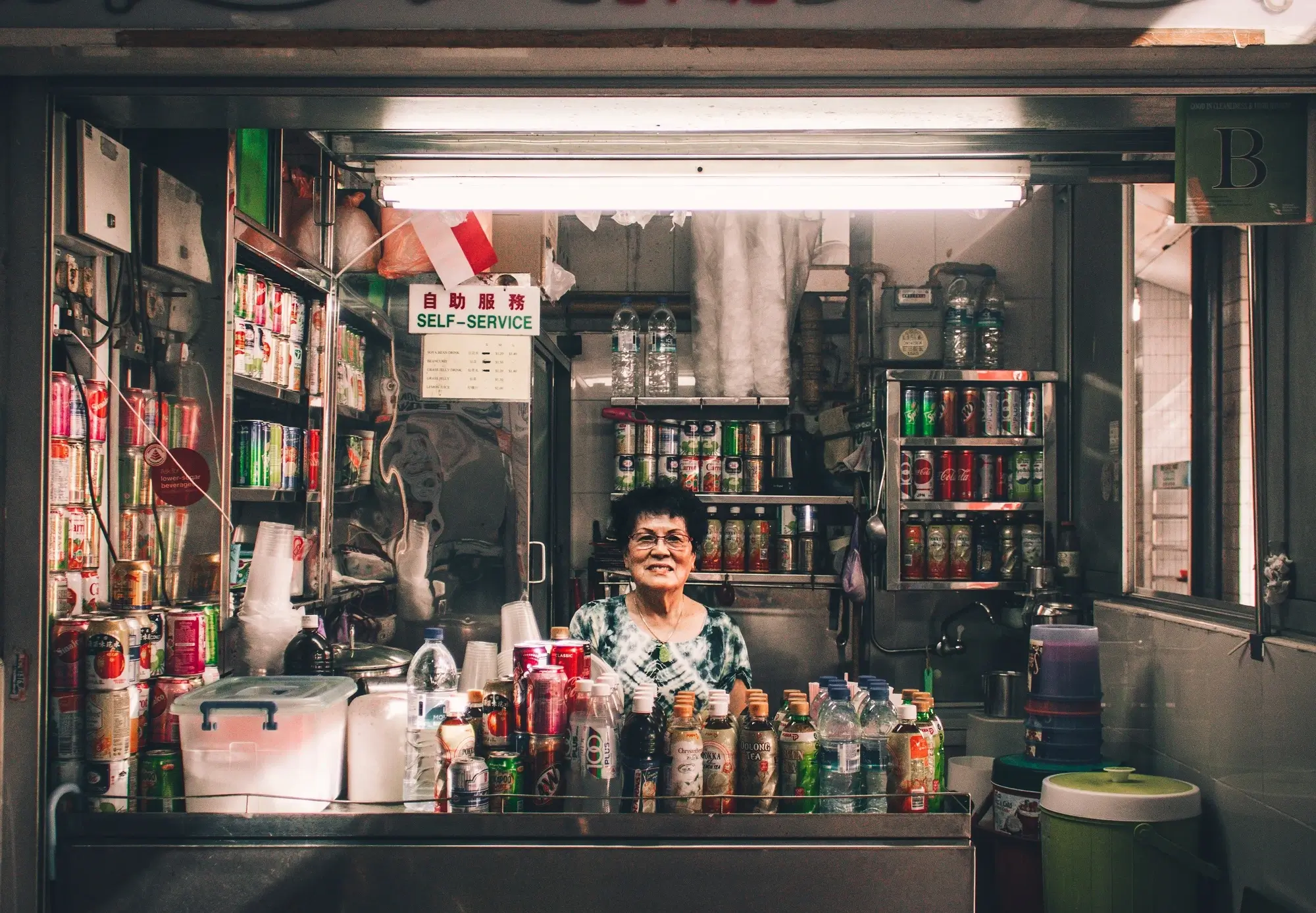 A vendor standing in front of the counter of her small beverage store.