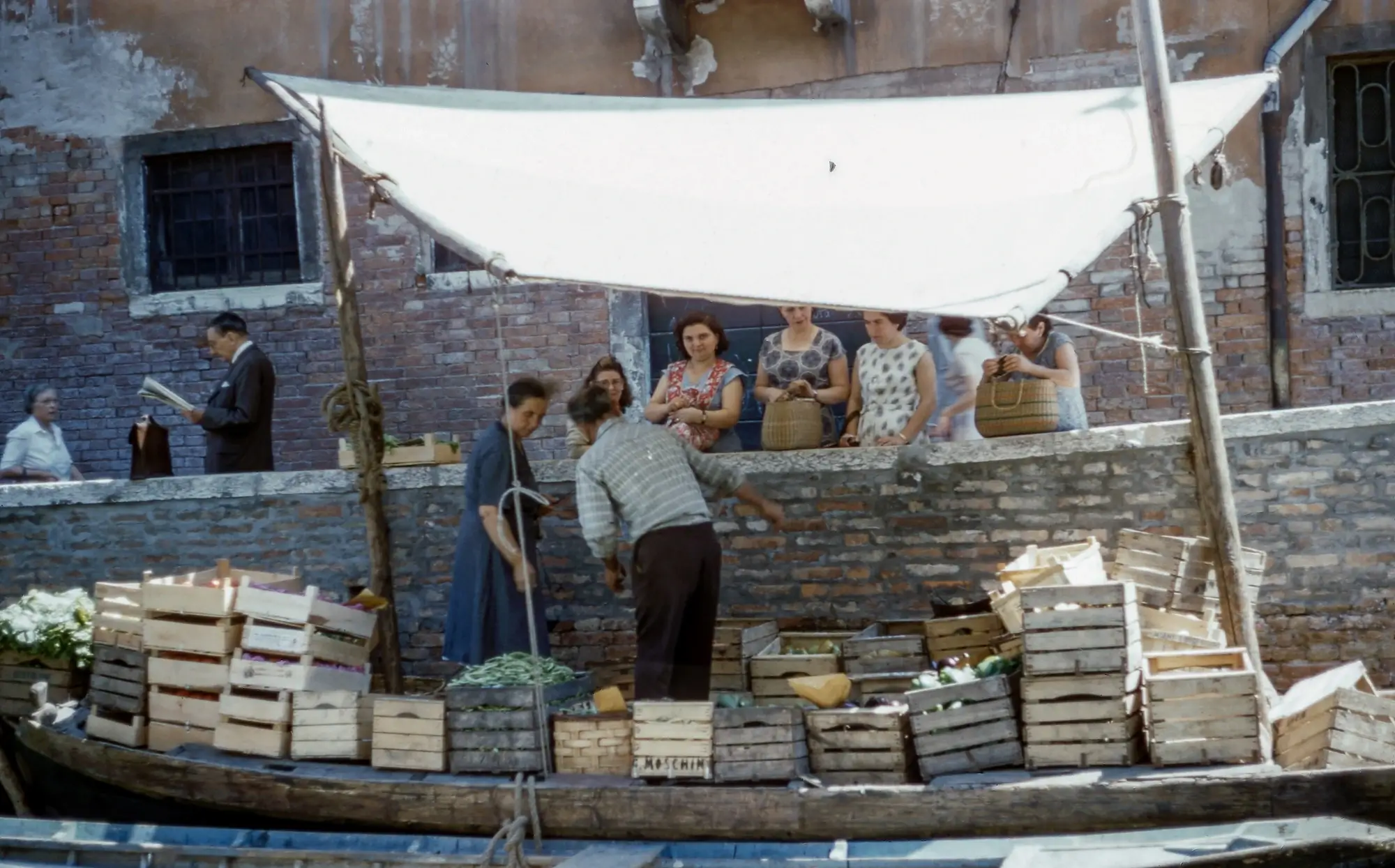 A vendor handing goods to his buyers from his floating store.