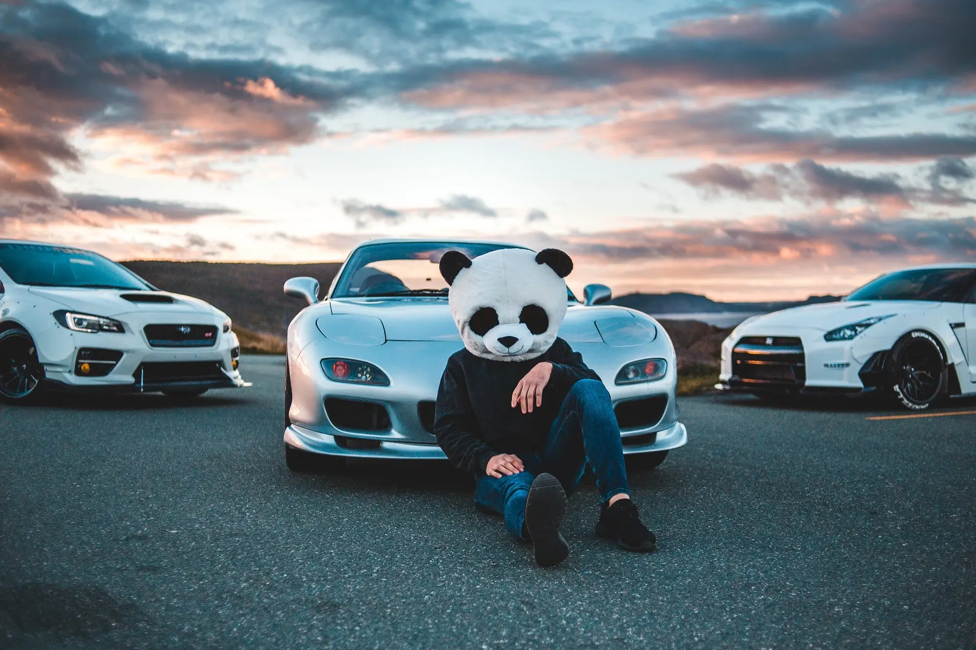 A man wearing a panda headpiece while sitting against a roadster, representing the concept of exempt fringe benefits.