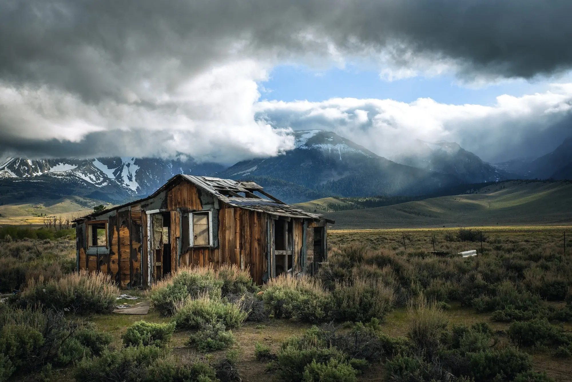 An old shack in an open field and set against icy mountains, representing the concept of living away from home allowance.