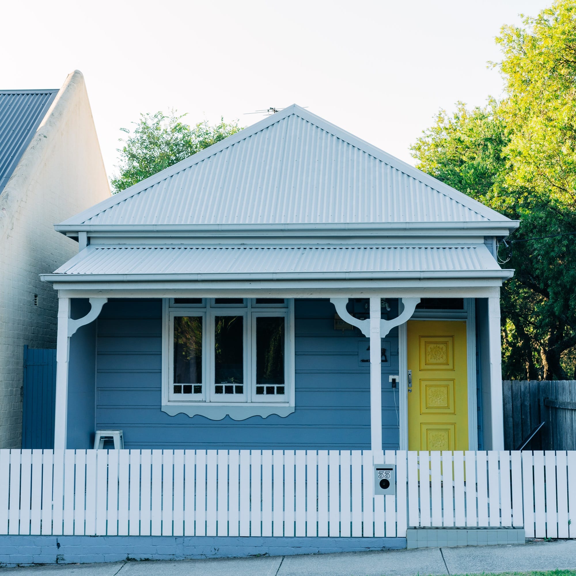 A blue house with a yellow door and a white picket fence, representing the concept of first home super saver scheme.