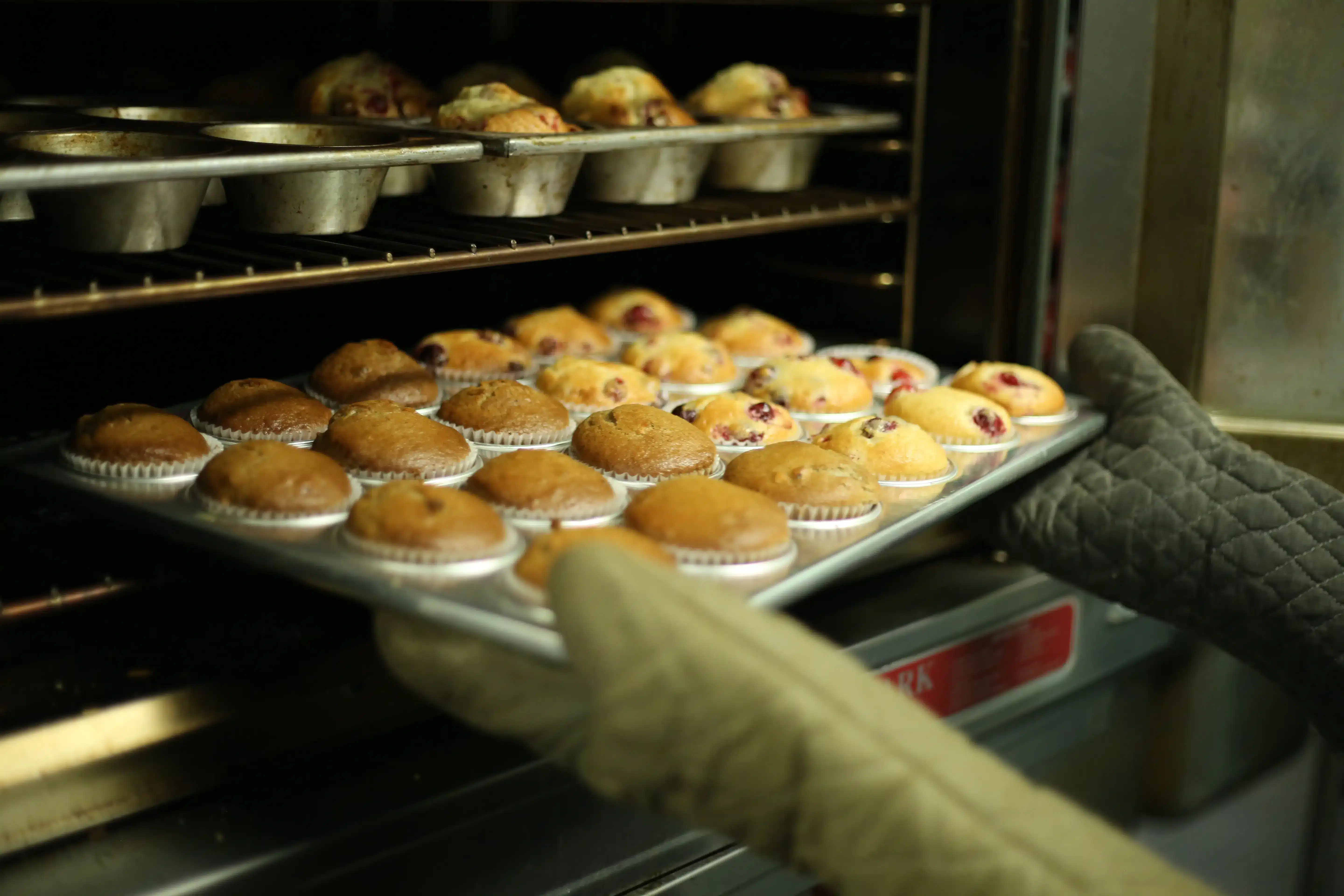 A baker pulling muffins out of an oven.