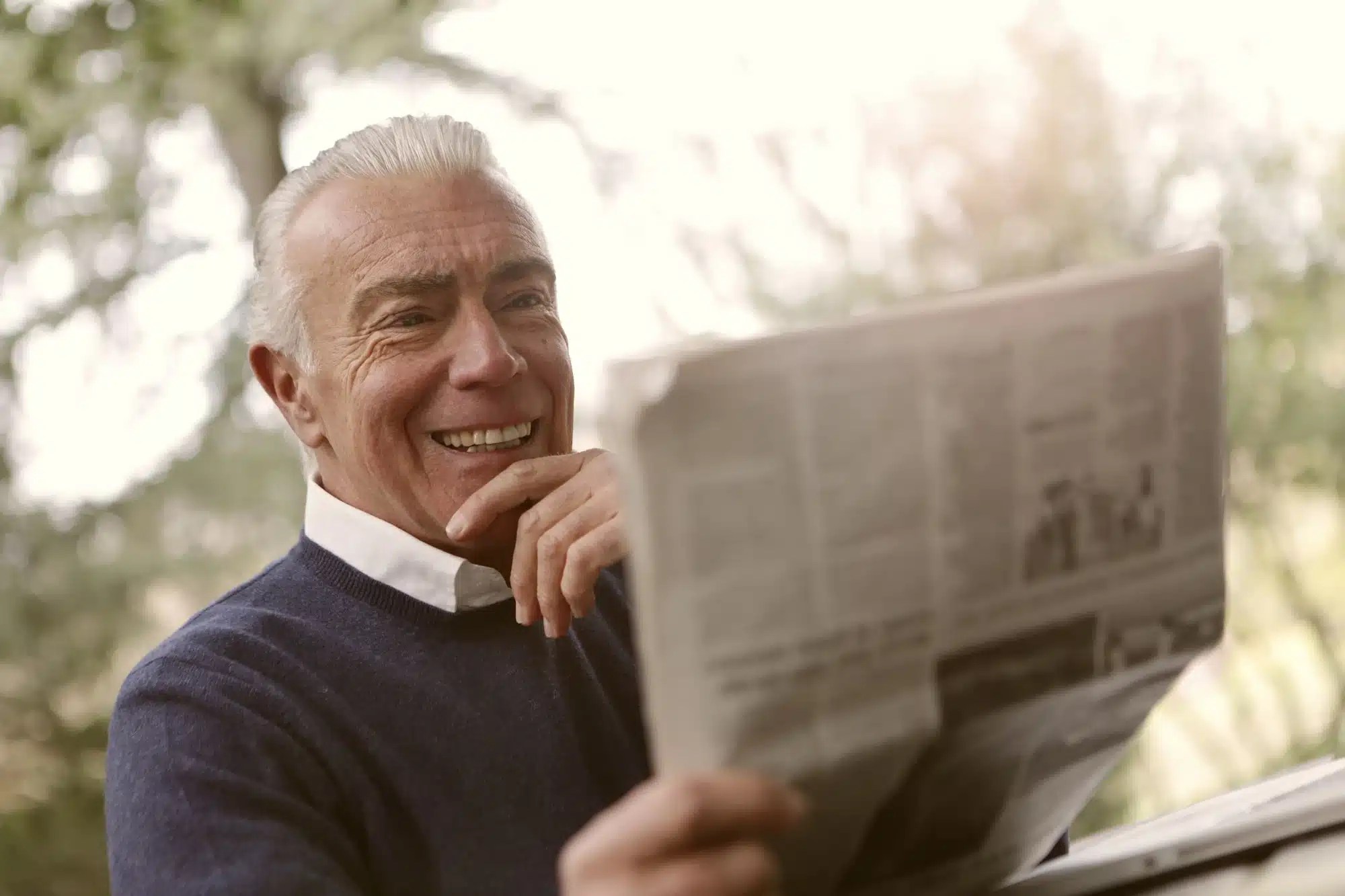 A retired man smiling while looking at the paper.
