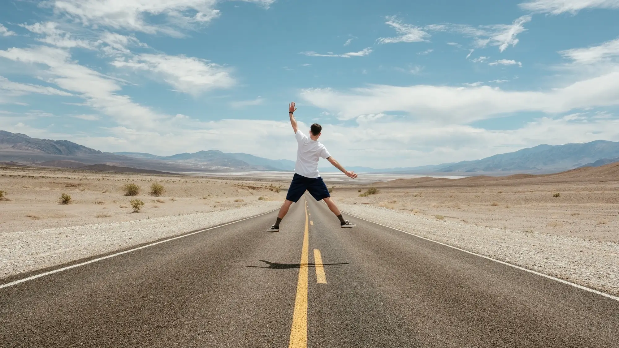 A man doing a jump shot in the middle of a desert road, representing the concept of working holiday maker.
